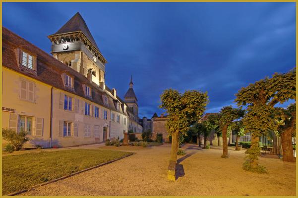 Photo de l'ancien tribunal et de l'ancienne prison de Chambon-sur-Voueize à la tombée de la nuit, sur la place Aubergier, avec les clochers de l'abbatiale Sainte-Valérie, dans le coeur historique du village au printemps.